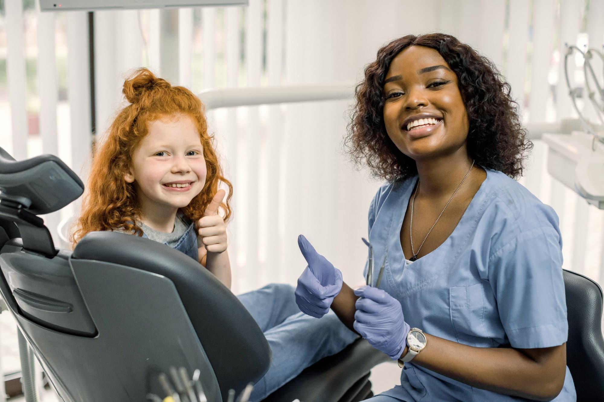 A dental hygienist with a young patient giving the thumbs up